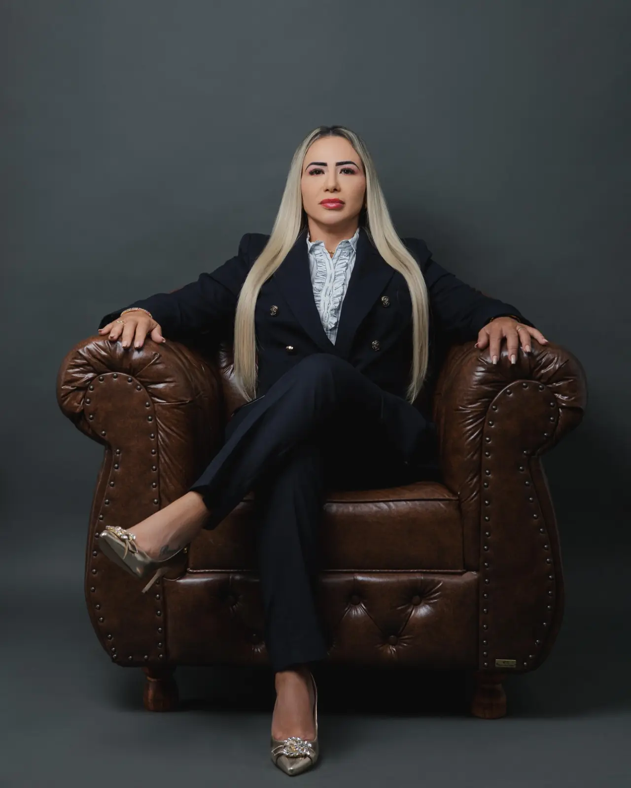 Amanda Barreto, advogada, sentada em poltrona de couro, vestindo terno azul-marinho